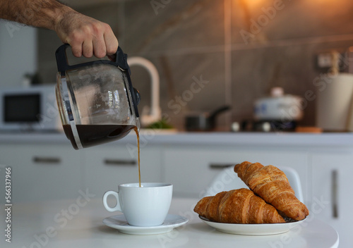 Fotobehang a man holds a teapot with coffee and pours into a white cup, a hot fresh drink,