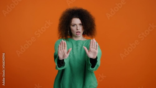 Determined young woman in green knitted sweater, showing STOP hand sign over orange color background photo