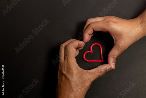 Manos formando corazón el fondo negro y corazones hechos en plastilina, concepto del día del amor y la amistad, san Valentín.