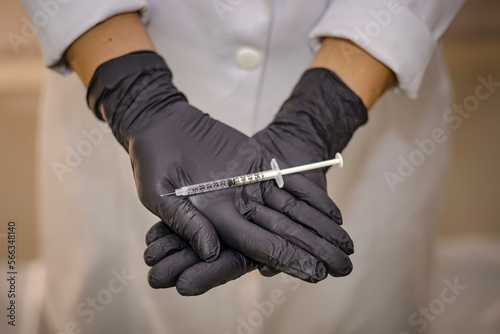 Sao Paulo, SP, Brazil - January 22 2023: Person in white coat and black gloves holding syringe with needle details. photo
