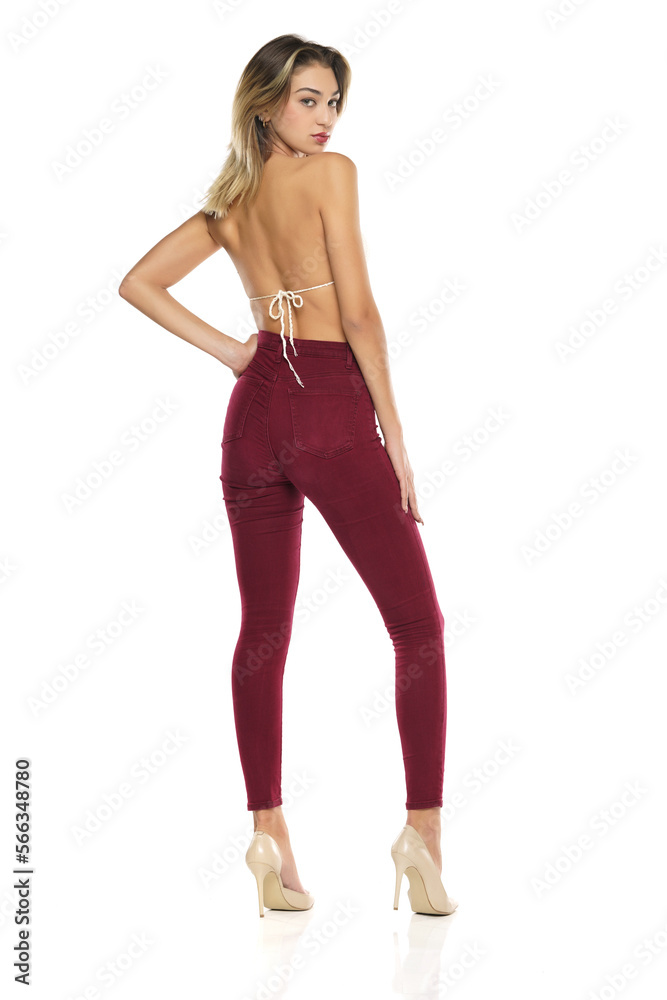 a young woman in burgundy jeans and top, and high heels shoes posing on a white background. Rear, back view a young woman in burgundy jeans and top, and high heels shoes posing on a white background. Rear, back view