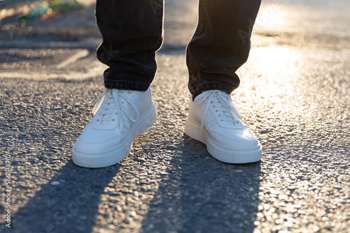Man in white sneakers shoes on asphalt at sunset. Men's shoes