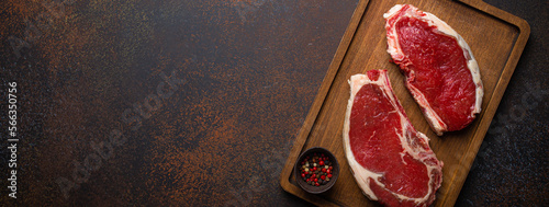 Panel kuchenny z motywem Two raw uncooked meat beef rib eye marbled steaks on wooden cutting board with seasonings on dark rustic background ready to be grilled from above, preparing dinner with meat, space for text