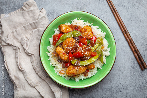 Asian sweet and sour sticky chicken with vegetables stir-fry and rice in ceramic bowl with chopsticks top view on gray rustic stone background, traditional Asian dish photo