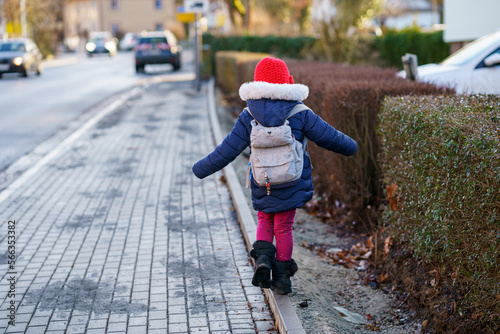 Cute little preschool girl with glasses on her the way to playschool. Healthy happy child walking to nursery school. Kindergarten kid with backpack going to day care on the city street, outdoors