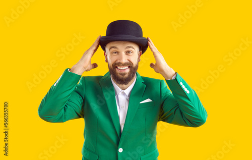 Portrait of cheerful smiling man in green jacket and black hat on orange background. Happy bearded man in stylish fashion suit celebrating St. Patrick's Day and smiling looking at camera.