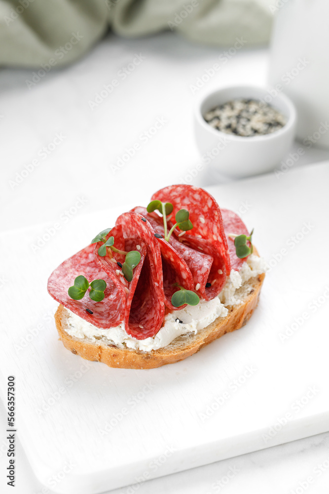 Sandwich, toast with cream cheese, sliced salami, sausage, microgreen on white cutting board. Snack, bruschetta.