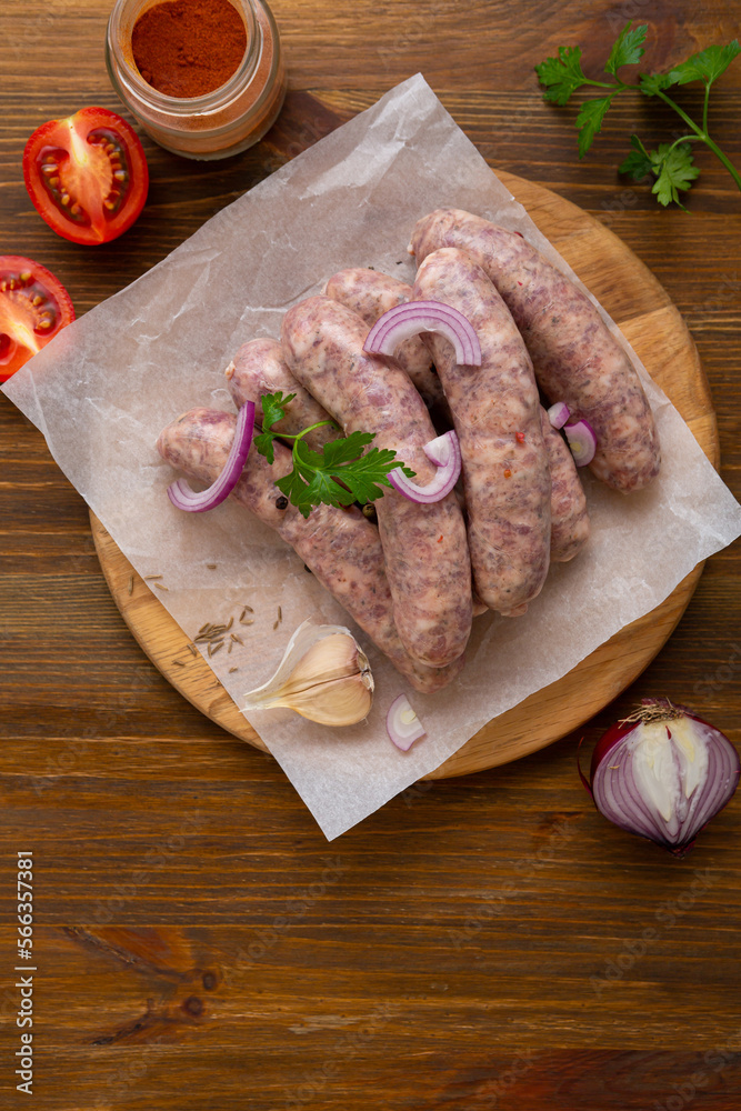 Several of uncooked bbq sausage on wooden board with spice onion tomato Several of uncooked bbq sausage on wooden board with spice onion tomato