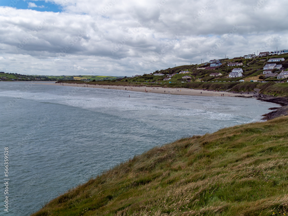 View of Inchydoney beach from the Cape of the Virgin Mary. Picturesque Irish seascape. A small European settlement on the seashore in summer. Green grass near body of water under cloudy sky