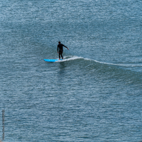 One man in a waterproof suit is surfing. Water sports. Man in black wet suit surfing on sea