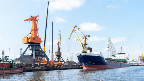 Vessel on which coal is loaded at seaport. Port cranes for loading coal onto ship, Kaliningrad, Russia. Coal on pier at seaport. Preparation for loading coal on ship photo