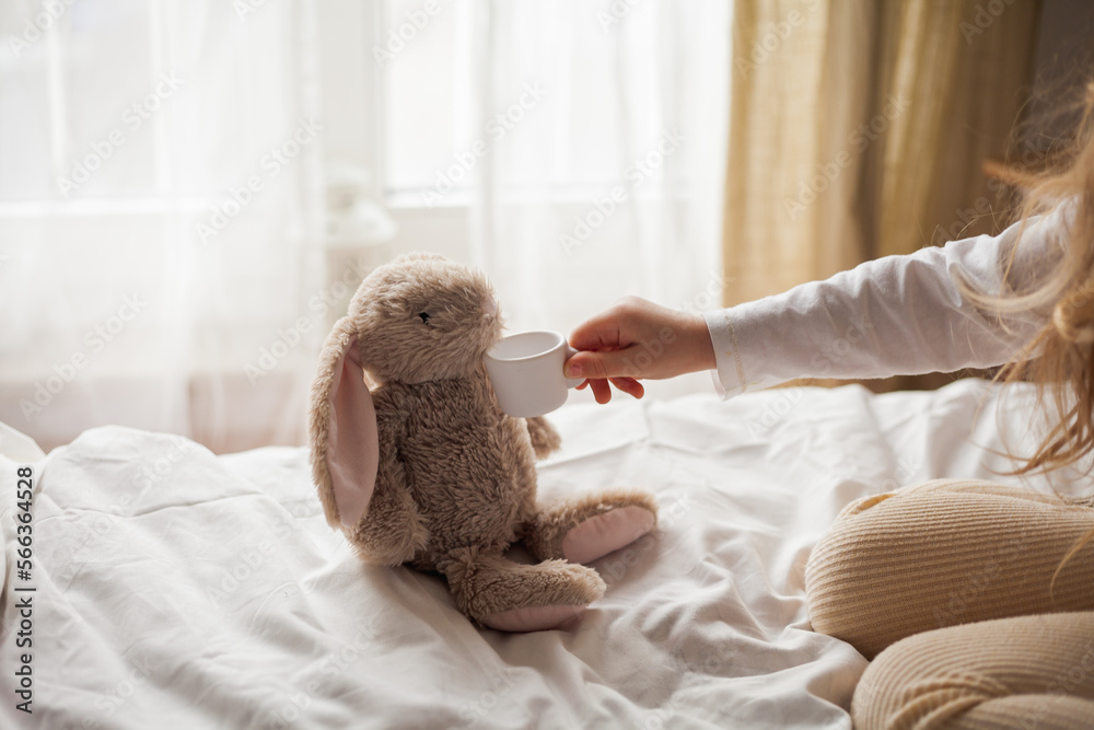 Curly-haired little blue-eyed girl of 4 plays with her plush rabbit in tea party. Children's room. Cosy. Curly-haired little blue-eyed girl of 4 plays with her plush rabbit in tea party. Children's room. Cosy.