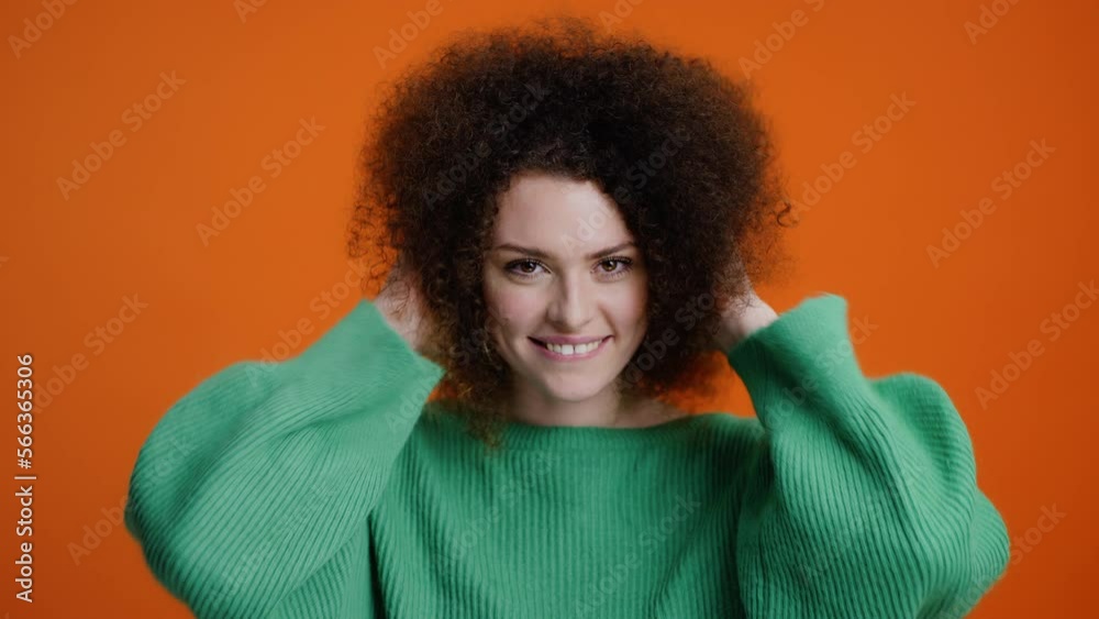 Attractive curly-haired woman admiring her appearance while looking at camera like into a mirror Attractive curly-haired woman admiring her appearance while looking at camera like into a mirror