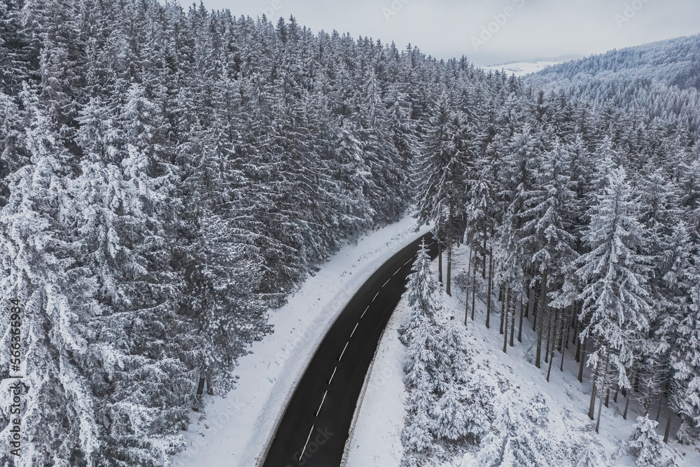 Snow-covered trees in the forest and asphalt road line in the mountains. Winter landscape in the mountains. Aerial drone panoramic photo. Snow-covered trees in the forest and asphalt road line in the mountains. Winter landscape in the mountains. Aerial drone panoramic photo.