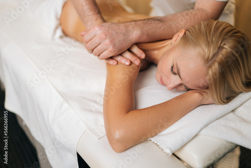 Cropped shot of unrecognizable professional male masseur therapist doing wellness beauty treatment to attractive blonde female lying on treatment table in spa salon. Concept of healthy lifestyle.