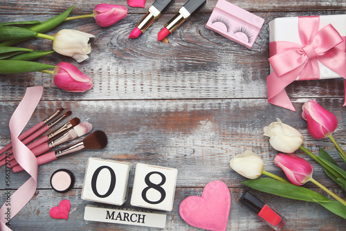 Flowers of tulips, cube calendar, cosmetics, makeup brushes and hearts, gift box, space for text on wooden background