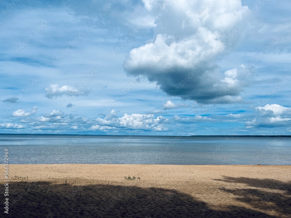 Wild sandy beach and very calm sea horizon, fluffy clouds in the bright sky