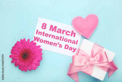 Gerbera flower, felt heart, gift box and card with text 8 March International Women's Day on blue background