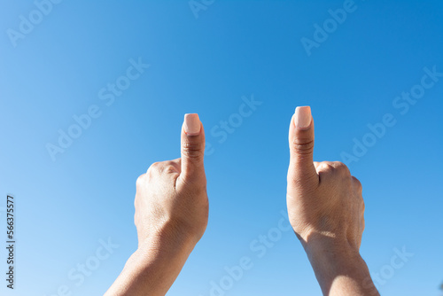 woman's hand showing thumbs up with blue sky background