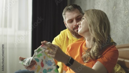 Happy pregnant Caucasian couple looking at baby clothes. Lovestyle of a happy family. A man and a woman are cooing and laughing. Waiting for a child. photo