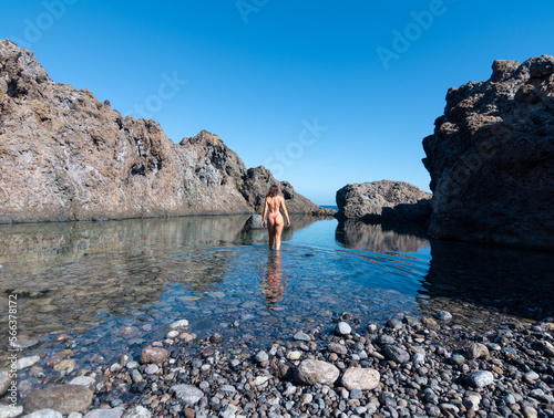 Young woman from behind in a bikini entering the water of a natural pool of volcanic rock in Tenerife