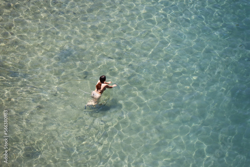 Aerial view to azure sea and girl in bikini swimming in transparent water. Beach vacation in summer
