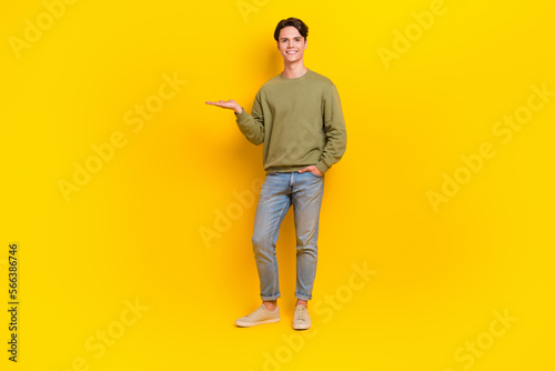 Full length photo of good looking man wear khaki clothes demonstrate empty space special offer isolated on yellow color background