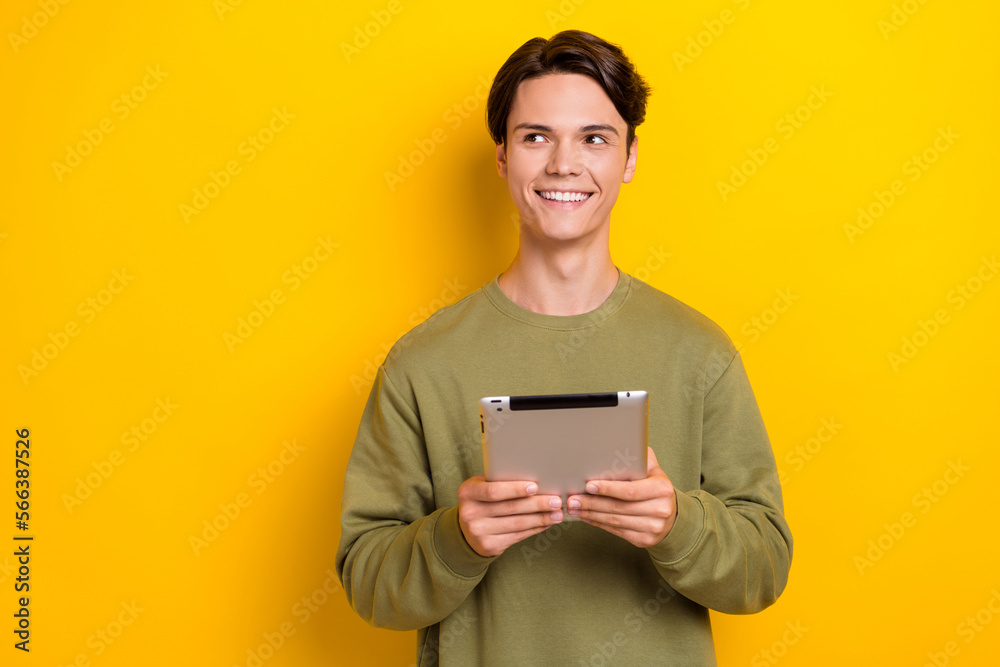 Photo of cheerful minded man hold tablet toothy smile look empty space isolated on yellow color background Photo of cheerful minded man hold tablet toothy smile look empty space isolated on yellow color background