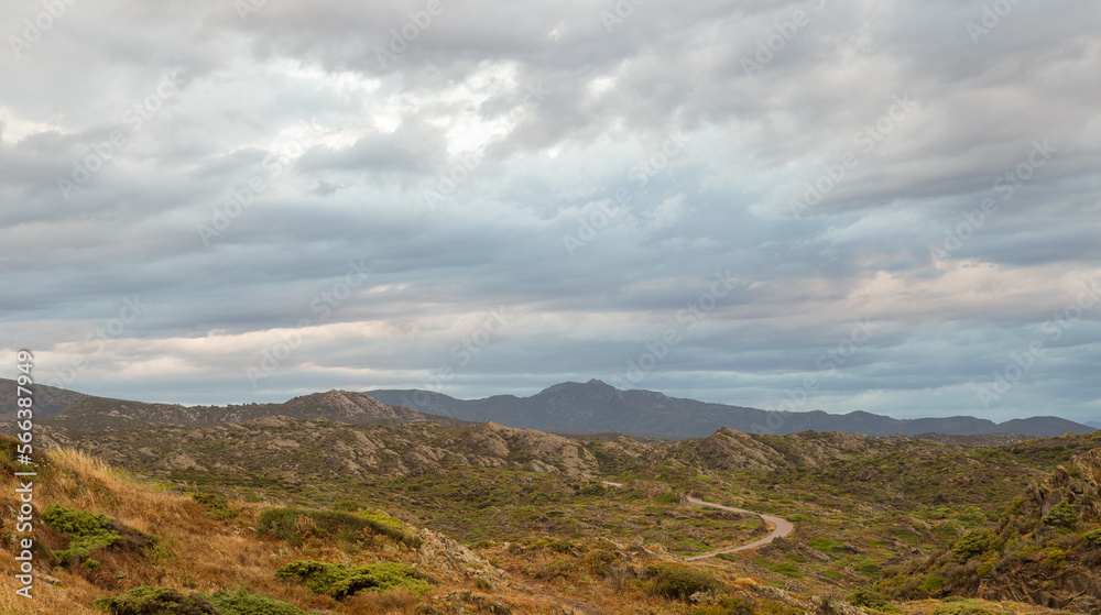 Panoramic view of the mountains of Cap de Creus a cloudy autumn day. There is a narrow winding road.