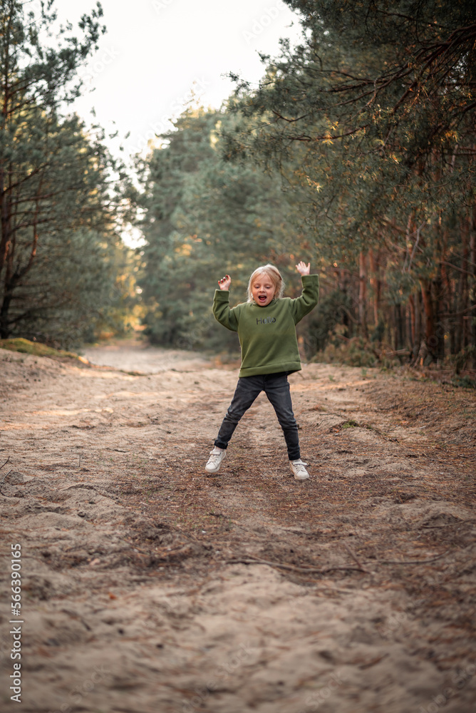 Little blonde girl dancing jumping on the sand in a pine forest