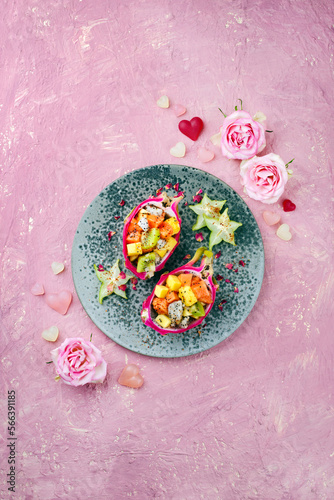 Traditionelle Valentinstag Fruchtsalat mit exotischen Fruchtstücken serviert in Drachenfrucht Schalen und dekoriert mit Sternfrucht auf einem Nordic Design Teller als Draufsicht mit Textfreiraum 