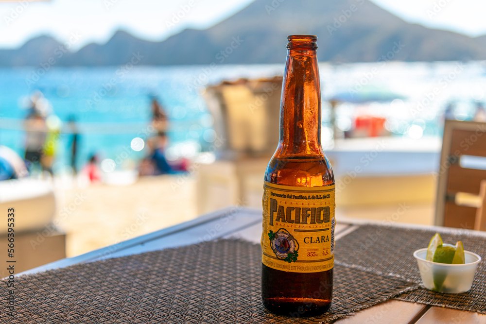 View of a bottle of Cerveza Pacífico Clara beer sitting on a waterfront  cafe table with the beach and sea of Cabo San Lucas, Mexico in view, on  January 6 2023. Stock-Foto