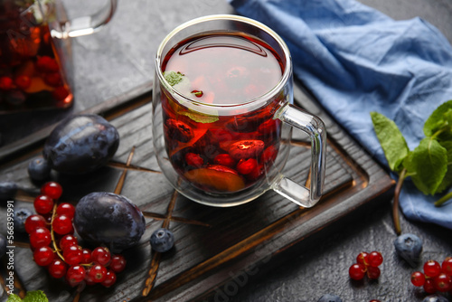 Board with glass cup of fruit tea and berries on dark background, closeup