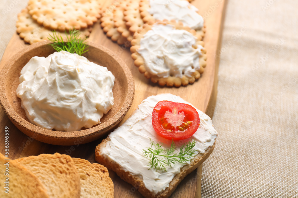 Wooden board with bowl of tasty cream cheese and crackers on table, closeup