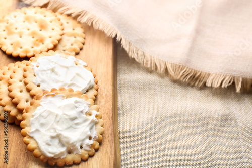 Wooden board of tasty crackers with cream cheese on fabric background, closeup