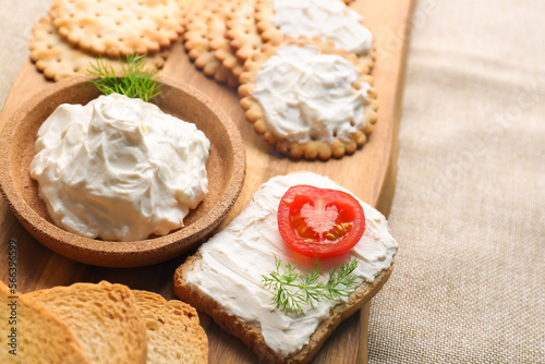 Wooden board with bowl of tasty cream cheese and crackers on table, closeup