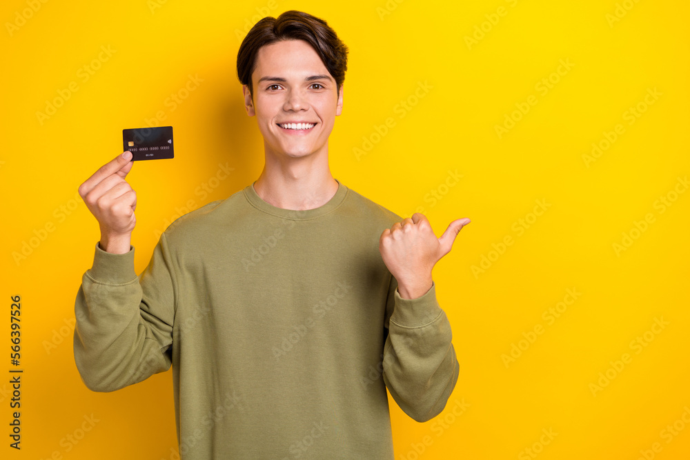 Portrait of positive attractive guy hand hold debit card direct finger empty space isolated on yellow color background Portrait of positive attractive guy hand hold debit card direct finger empty space isolated on yellow color background