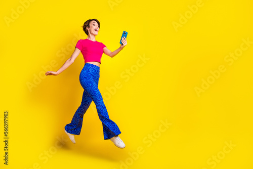Full length photo of positive cute lady user walk empty space speaking modern device gadget isolated on yellow color background © deagreez