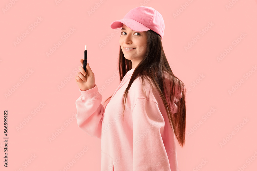 Young woman in cap with disposable electronic cigarette on pink background Young woman in cap with disposable electronic cigarette on pink background