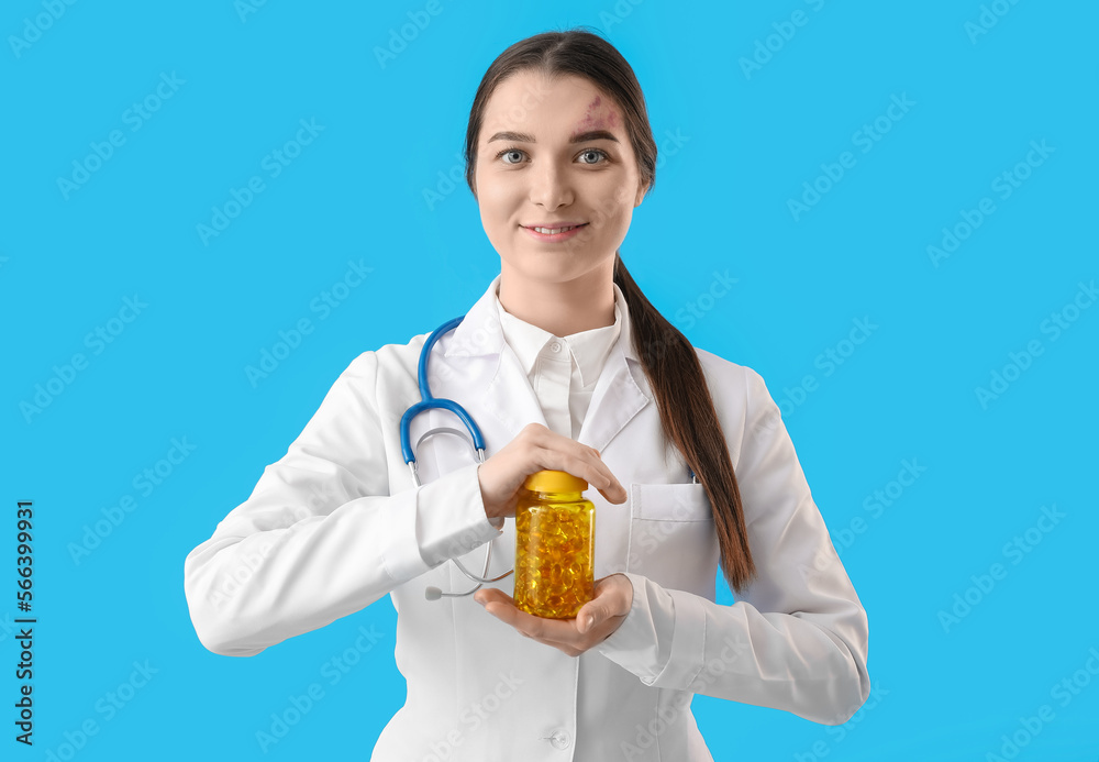 Female doctor with bottle of vitamin supplements on blue background