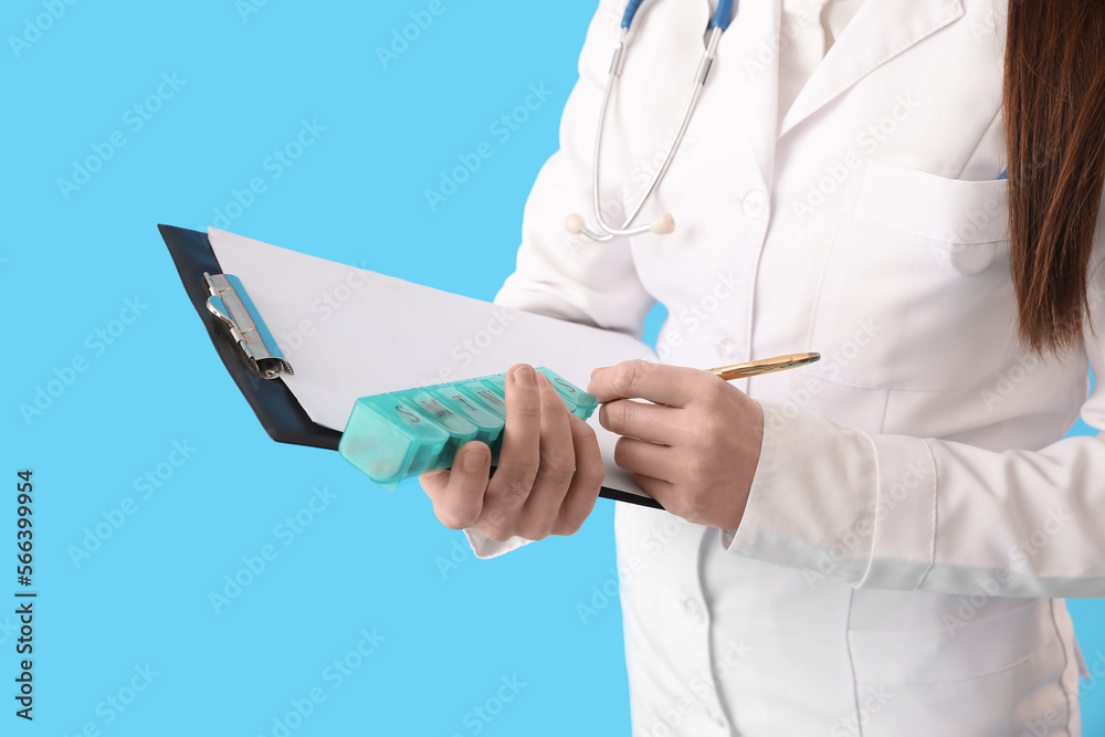 Female doctor with container of vitamin supplements and clipboard on blue background, closeup Female doctor with container of vitamin supplements and clipboard on blue background, closeup