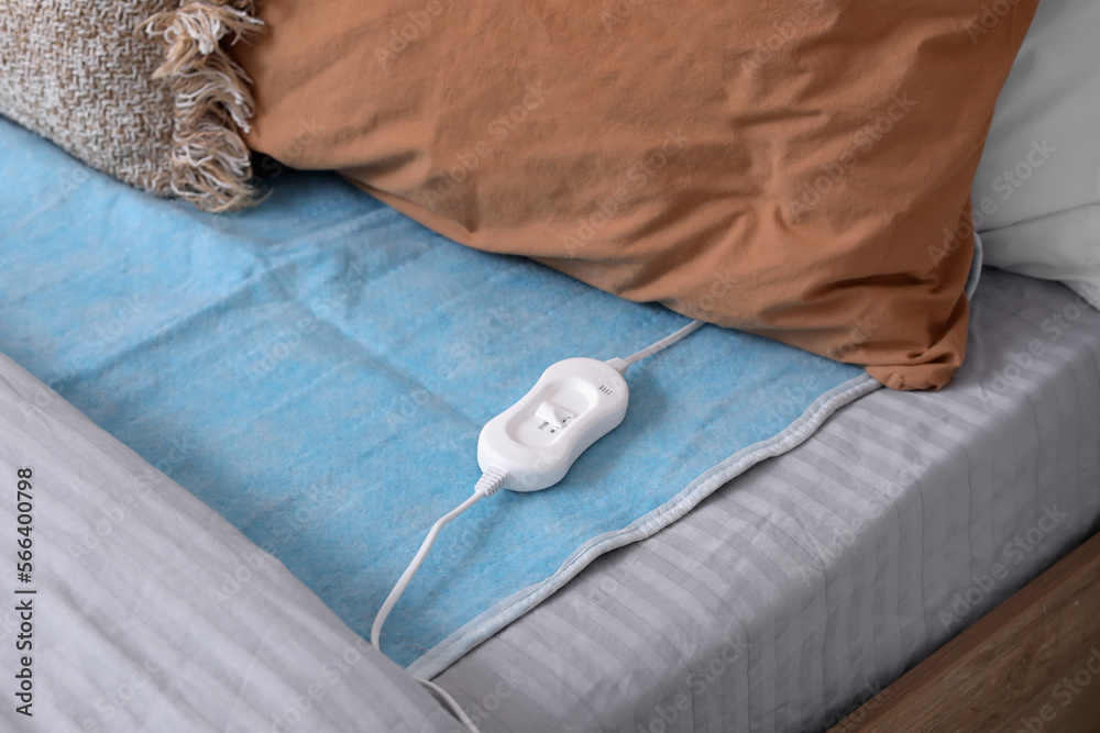 Electric heating pad with controller on bed in room, closeup