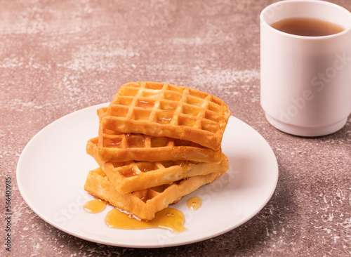 Delicious Belgian waffles with honey served on white plate and brown background, cup of black tea, rustic concept.