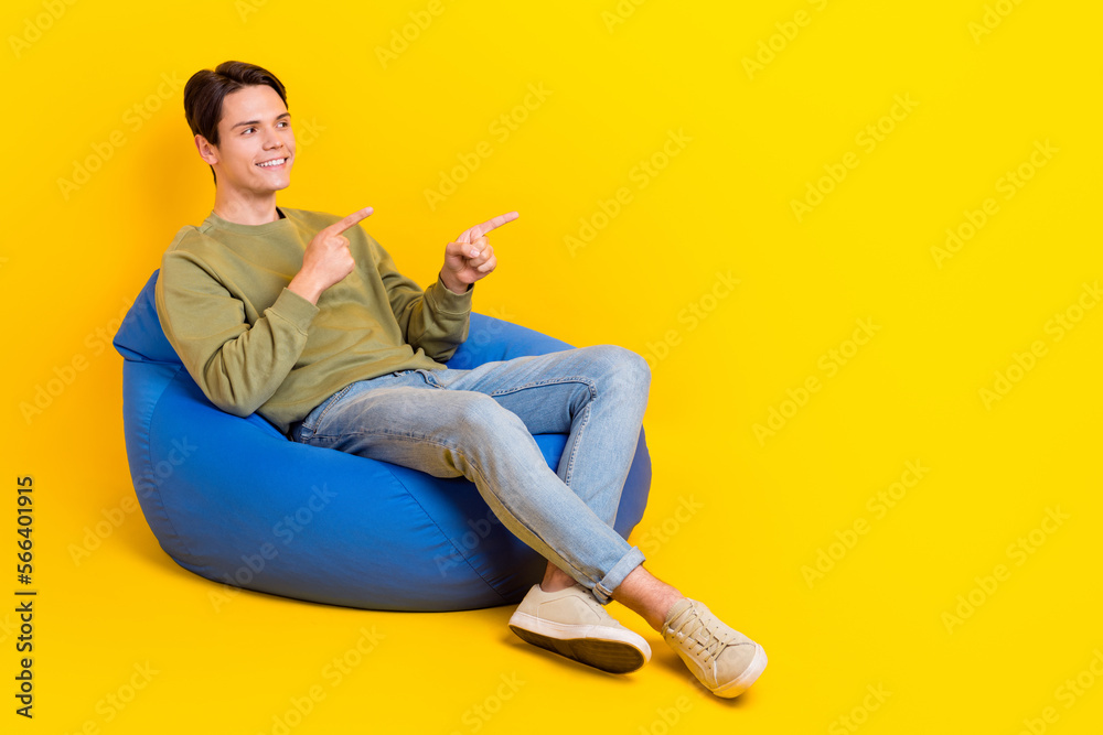 Full size photo of nice satisfied person sit comfy bag look direct fingers empty space isolated on yellow color background
