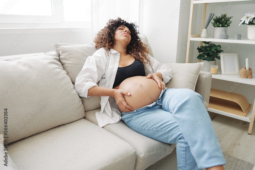 Pregnant woman headache lies at home in a shirt and jeans on the couch fatigue and heaviness in the last month of pregnancy before childbirth, motherhood difficulties, nausea Pregnant woman headache lies at home in a shirt and jeans on the couch fatigue and heaviness in the last month of pregnancy before childbirth, motherhood difficulties, nausea