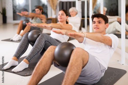 Sporty energetic males and females doing exercises with pilates ball during group training at gym. Fitness concept.