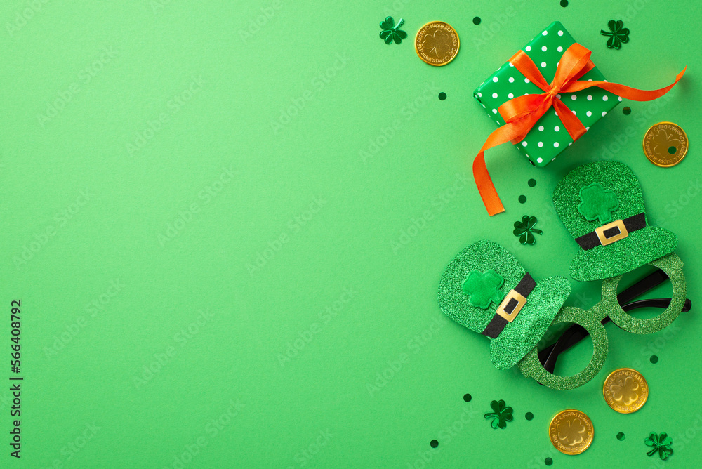 Naklejka premium Saint Patrick's Day concept. Top view photo of hat shaped party glasses green giftbox with orange ribbon bow gold coins and shamrock shaped confetti on isolated green background with copyspace