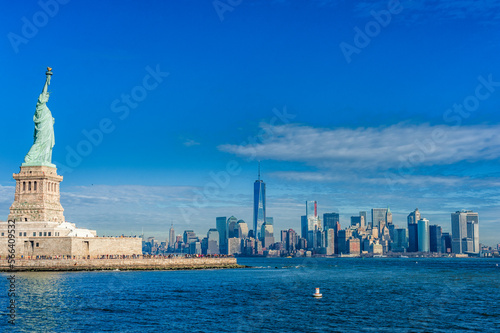 Statue of Liberty on Liberty Island and New York City Manhattan downtown skyline with skyscrapers and blue sky © Mindaugas Dulinskas
