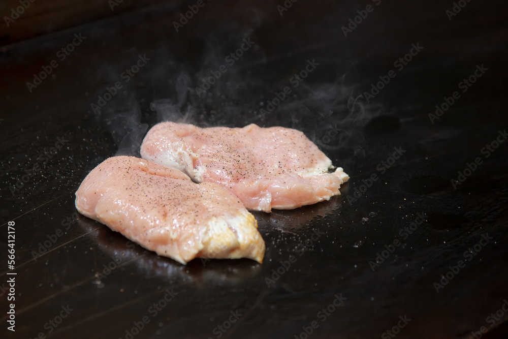 A view of some raw chicken breast cooking on a restaurant griddle surface.