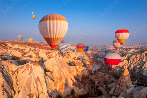 Sunrise in Cappadocia with colorful hot air balloons fly in blue sky over deep canyons, valleys. Travel Turkey landscape